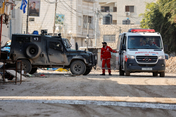 A man stands between an ambulance and an Israeli military vehicle, in Jenin